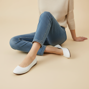 Person wearing blue jeans and white shoes sitting on a beige surface